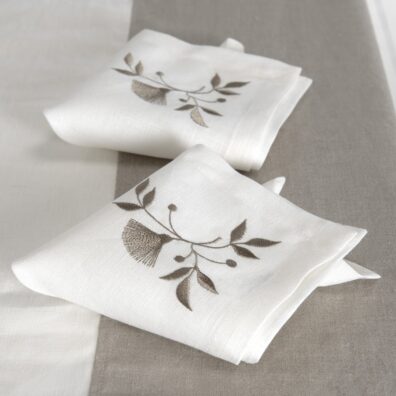 Weiße Leinenserviette mit bestickter beiger Blume und Blätterchen in einer Ecke