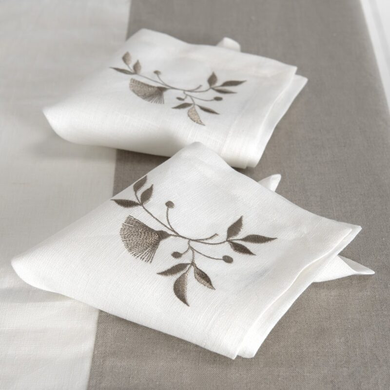 Weiße Leinenserviette mit bestickter beiger Blume und Blätterchen in einer Ecke